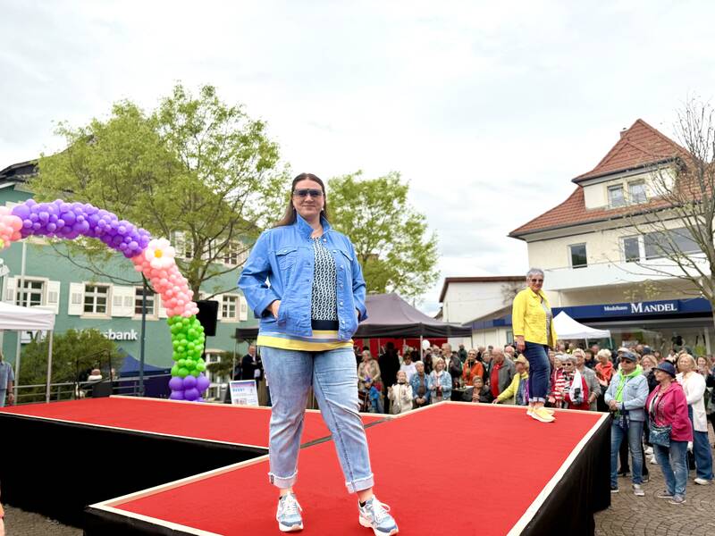 Eine Frau läuft über einen roten Laufsteg im Freien (Lammplatz, Bad Krozingen im Frühling), umgeben von einem Publikum und einem ballonverzierten Eingang.