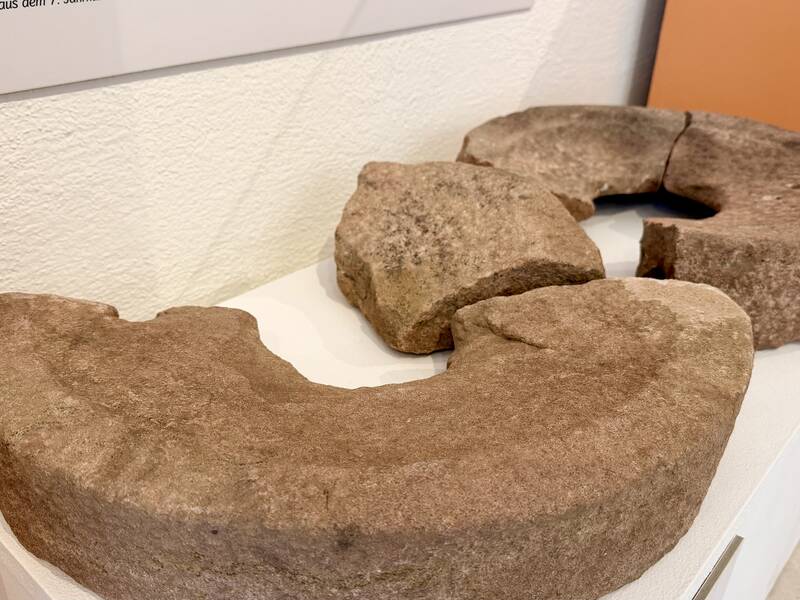 Drei große, bogenförmige Steinteile liegen auf einem Tisch und bilden gemeinsam einen unvollständigen Ring.