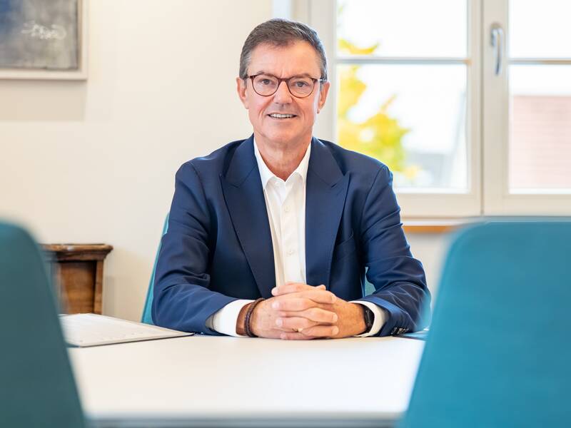 Ein lächelnder Mann, Oberbürgermeister Volker Kieber in einem blauen Anzug, sitzt an einem Tisch vor einem Fenster.