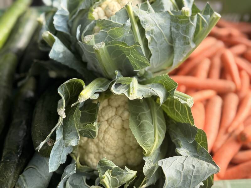Ein Blumenkohl mit grünen Blättern liegt neben einem Haufen Möhren.