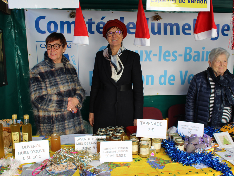 Drei Mitglieder des Vereins Verbindungen International Bad Krozingen e.V. stehen am Weihnachtsmartstand auf dem Christkindlemarkt Bad Krozingen.