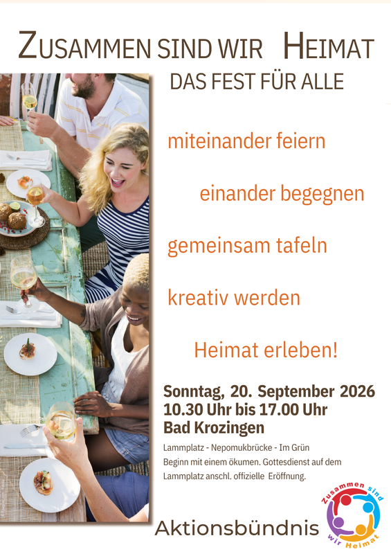 Eine Gruppe von Menschen sitzt lachend an einem gedeckten Tisch bei einem Fest mit dem Motto "Zusammen sind wir Heimat".